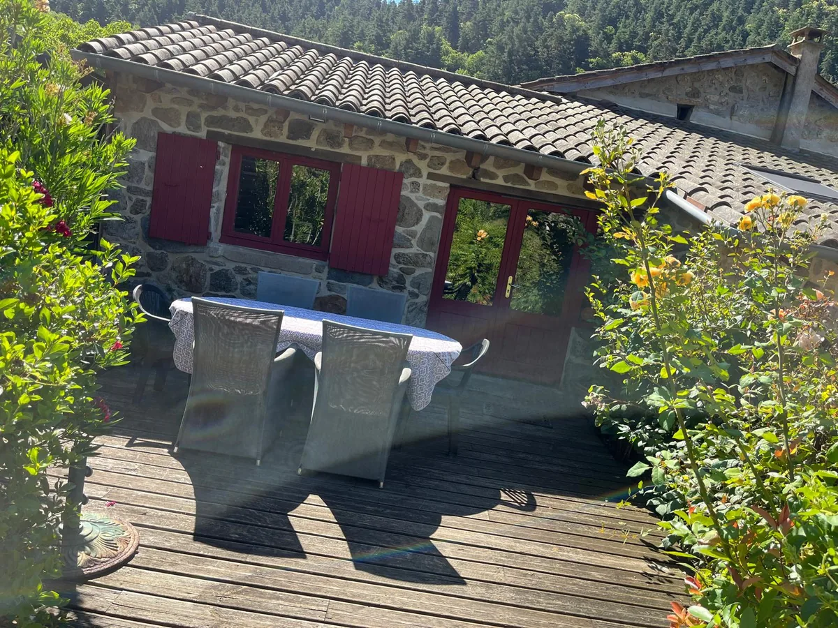 Terrasse en bois et façade en pierre aux volets rouges du gîte les Vérag
